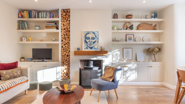 Ein modernes Wohnzimmer mit einer Couch, einem Couchtisch und einem Fernseher. Es gibt Bücherregale, einen Kamin und Dekorationselemente.