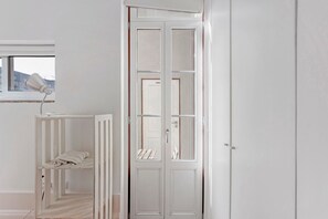 Ein Zimmer mit Reisebett, weißem Kleiderschrank und Fenster.