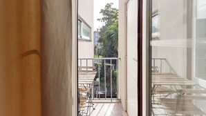 Un couloir étroit donnant sur un balcon agrémenté de tables et de chaises, muni d’une rambarde en métal et d’un escalier menant à un niveau supérieur.