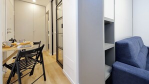 A modern living room with a blue sofa, a dining table with chairs, and a kitchen area with cabinets and a window. - 4BNB - Marmorata Urban Nest (Rome)