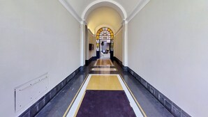 A long, narrow hallway with a tiled floor, white walls, and a central archway leading to another room. - 4BNB - Marmorata Urban Nest (Rome)