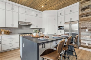A modern kitchen with white cabinets, a central island with bar stools, stainless steel appliances, and a wooden ceiling. - NEW! | Int Design | AC | Hot Tub | Backyard Oasis! (Flagstaff)