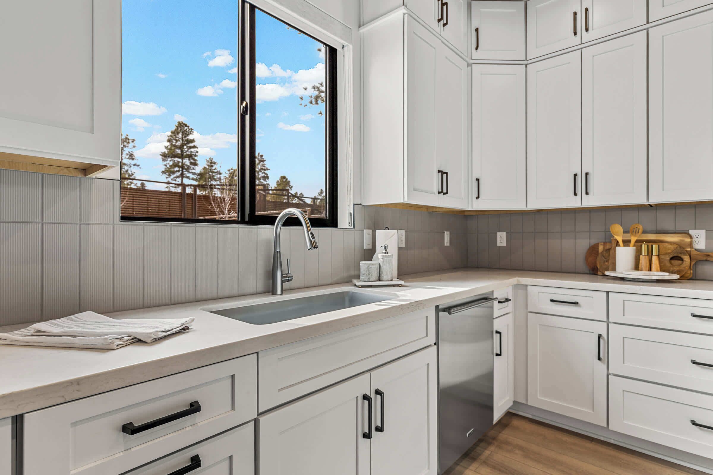A modern kitchen with white cabinetry, a stainless steel sink, and a window with a view of trees and sky.