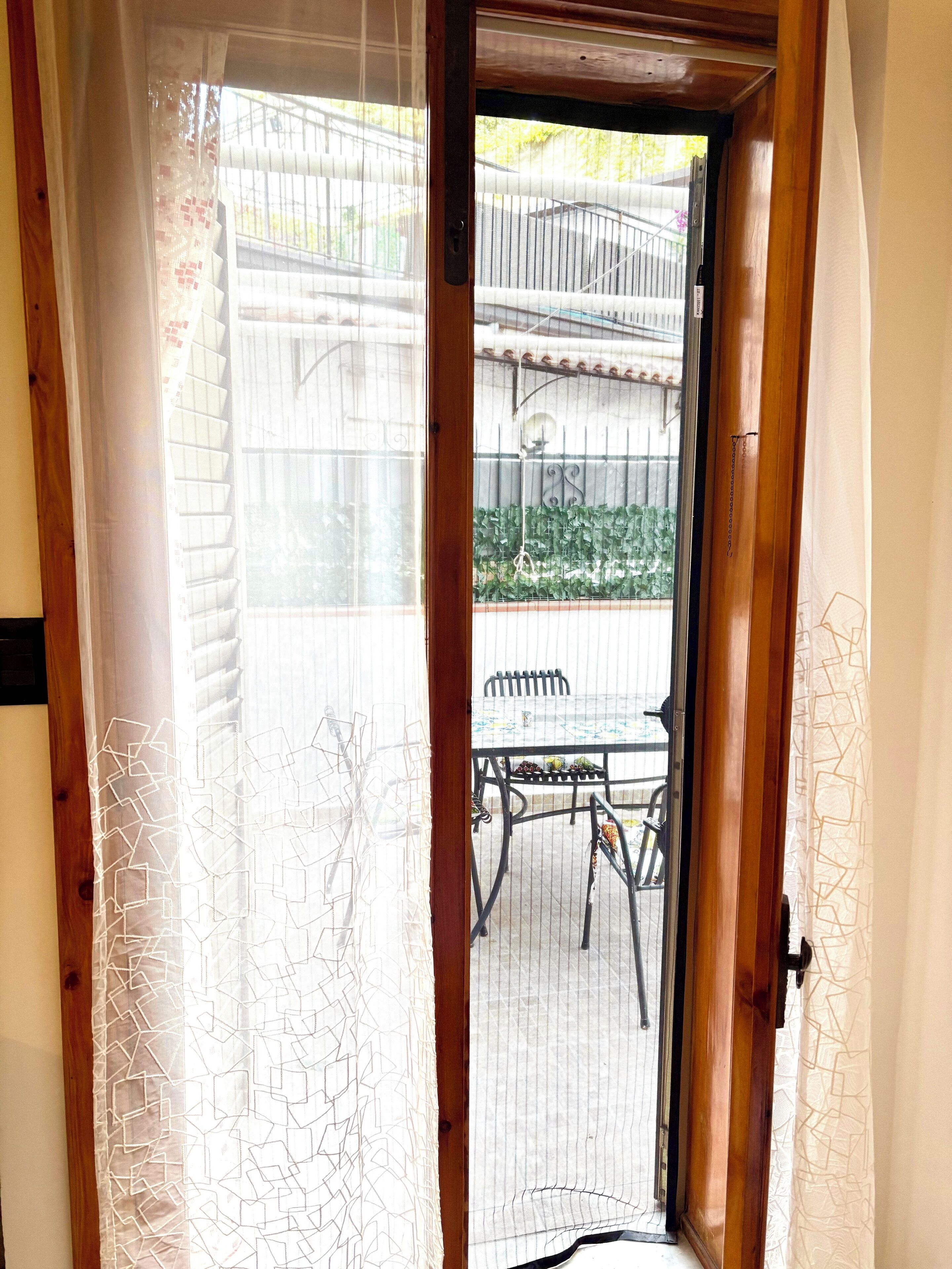 Une porte en bois avec un panneau de verre, qui donne sur un patio extérieur équipé d’une table et de chaises.