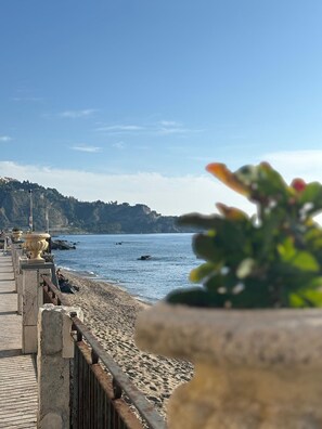 A coastal walkway with a rocky beach, a clear sky, and distant hills. - Apartment with an outdoor patio and parking space (Giardini Naxos)