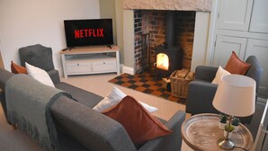 En stue med pejs, et fjernsyn der viser 'NETFLIX', og et ternet tæppe.
