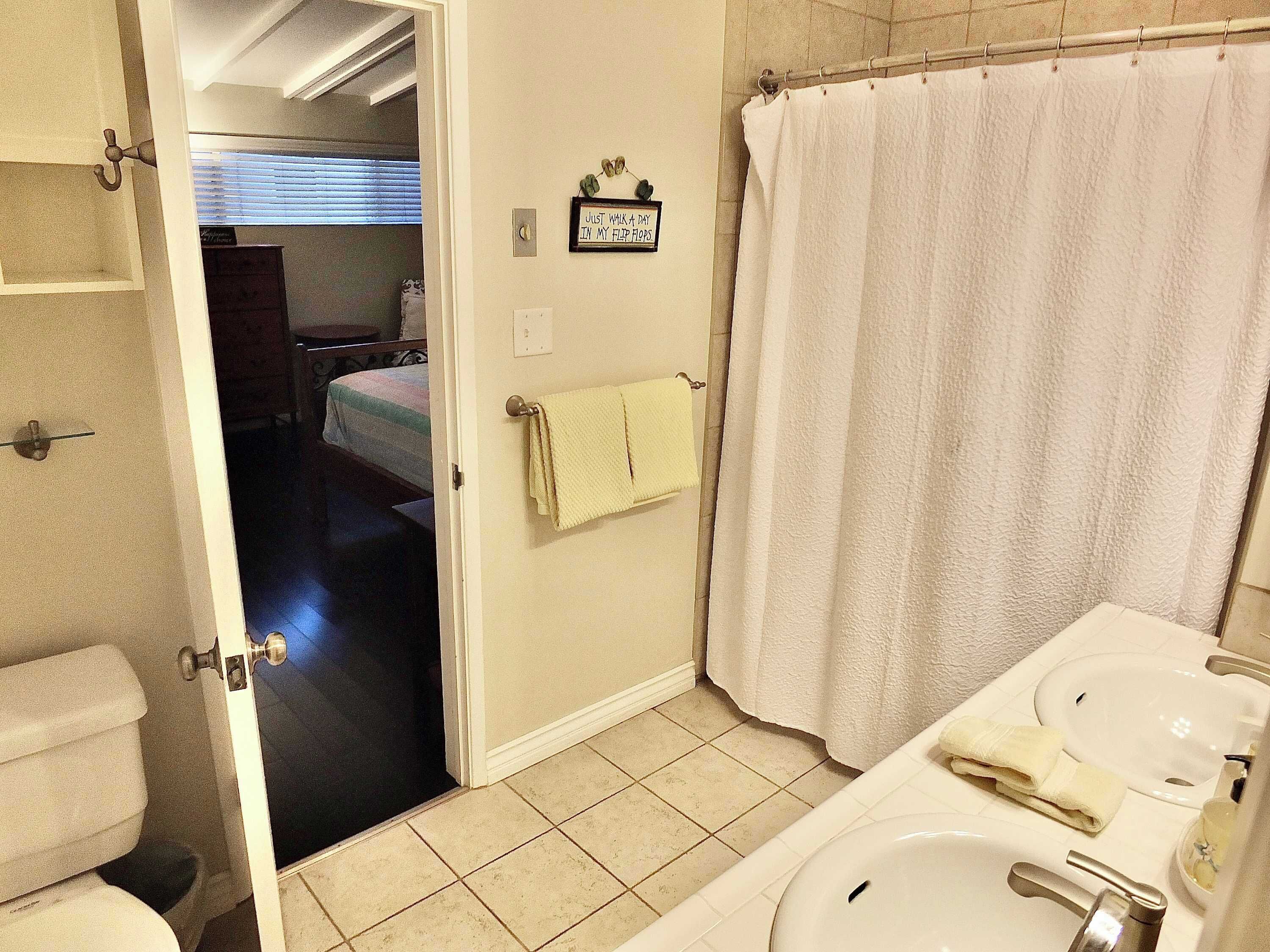 A bathroom with a toilet, sink, and shower curtain. There is a towel hanging on the wall and a sign that reads "Just Walk in My Flap."