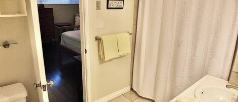 A bathroom with a toilet, sink, and shower curtain. There is a towel hanging on the wall and a sign that reads "Just Walk in My Flap."