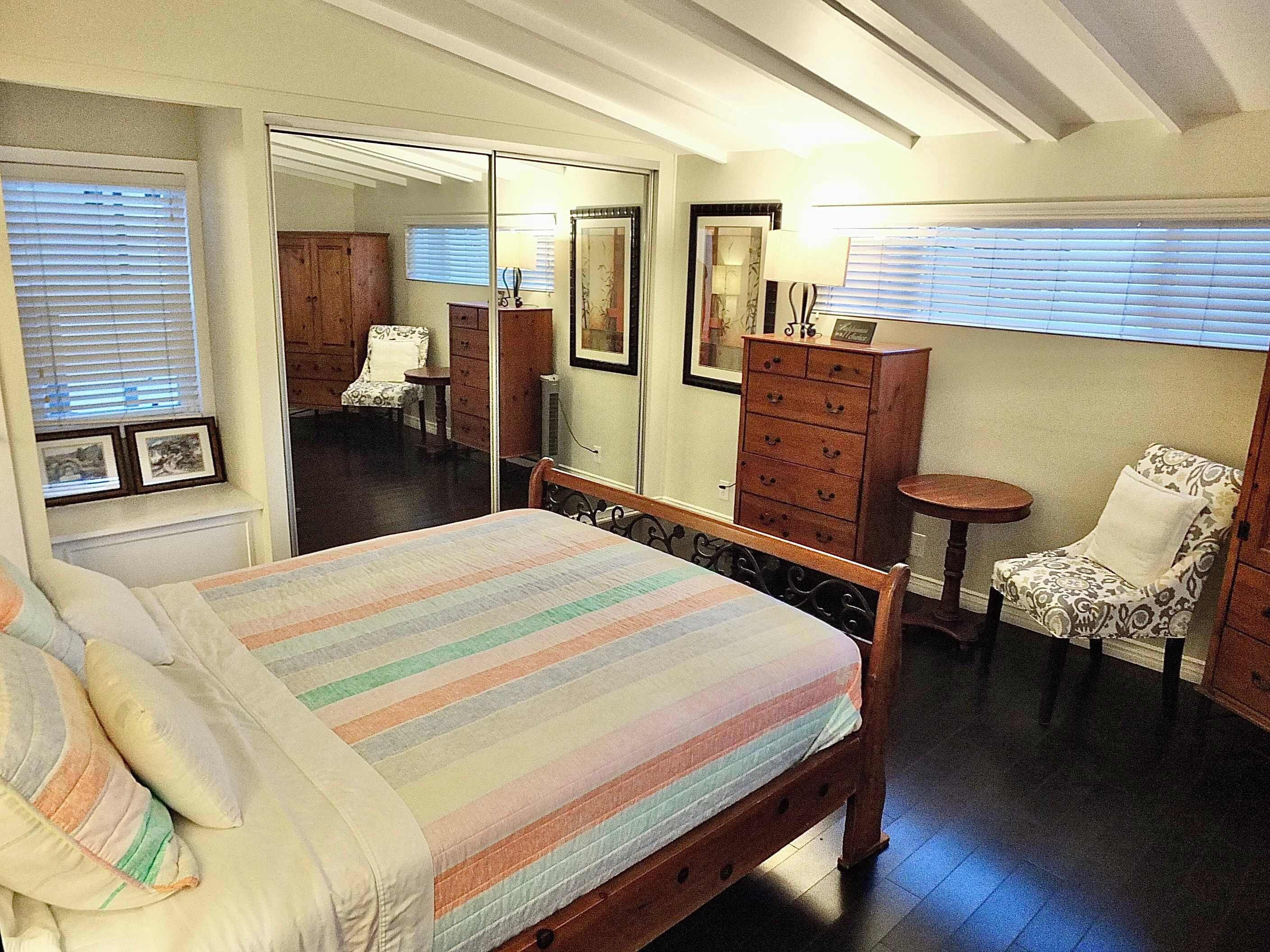 Un dormitorio con cama, una silla, un tocador y un espejo.