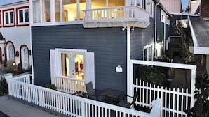 Una casa a due piani con un balcone, un piccolo portico e un recinto in legno bianco.