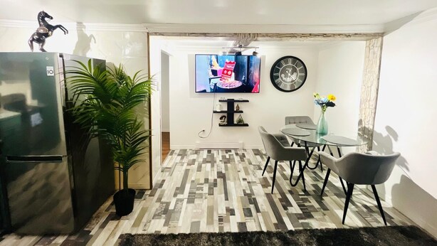 Une cuisine moderne équipée d’un réfrigérateur, d’un coin repas avec une table et des chaises, d’une plante en pot et d’un téléviseur fixé au mur.