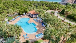 Vista aérea de un complejo turístico con una gran piscina rodeada de palmeras y sillas de descanso.