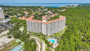 Un gran hotel de varios pisos, rodeado de abundante vegetación y una zona de piscina.