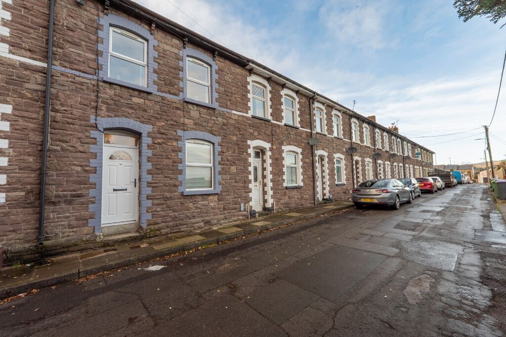 A row of terraced houses with a paved street and parked cars.