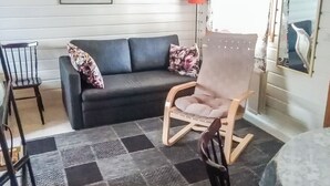 Una sala de estar con un sofá gris oscuro, una mecedora de madera, una pequeña mesa de madera y un tapete estampado.