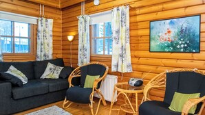 Ein gemütliches Blockhaus-Interieur mit einer Couch, zwei Korbstühlen, einem kleinen Tisch und einer Heizung.