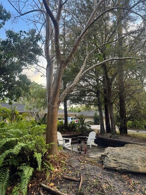 A patio area with two white chairs, a fire pit, and a large rock. - NEW! Private Tennis Ranch in Lake Worth - Serene & Tranquil Retreat, BBQ & Pool! (Greenacres)