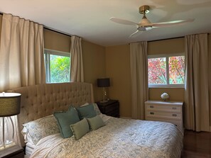 A bedroom with a tufted headboard, a bed with patterned bedding, a nightstand with a lamp, a dresser, and a ceiling fan. - NEW! Private Tennis Ranch in Lake Worth - Serene & Tranquil Retreat, BBQ & Pool! (Greenacres)