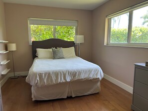 Une chambre à coucher avec un lit, des lampes de chevet, une fenêtre donnant sur un paysage verdoyant et une commode.