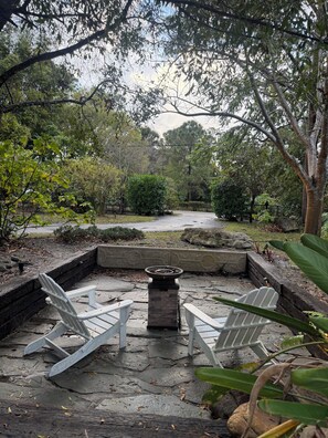 Ein Garten mit einer Steinsitzbank, einem Feuerkorb und einem Weg, der durch das Grün führt.