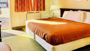 A hotel room with a bed, a desk, a chair, a lamp, and a window with curtains.