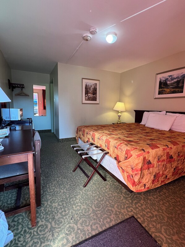 Une chambre d’hôtel avec un lit, un bureau, une chaise, une lampe et deux tableaux encadrés au mur.