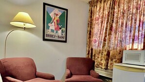 A room with two armchairs, a small table, a lamp, a framed picture, a microwave, and a curtain.