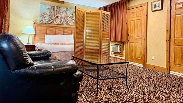 A hotel room with a bed, a black leather chair, a small table, and a patterned carpet.