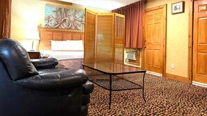 A hotel room with a bed, a black leather chair, a glass table, a wooden wardrobe, and a painting on the wall.