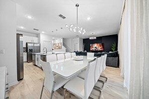 A modern kitchen with white cabinets, a stainless steel refrigerator, and a dining area with a glass table and white chairs. - 8BR house sleeps 24 with spa and private pool (Kissimmee)