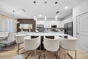 A modern kitchen with a central island, white bar stools, stainless steel appliances, and pendant lighting. - 8BR house sleeps 24 with spa and private pool (Kissimmee)