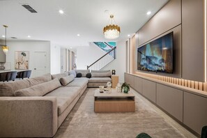 Ein modernes Wohnzimmer mit einem Ecksofa, einem Couchtisch und einem großen Fernseher an der Wand.