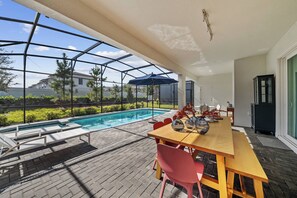 Ein überdachter Außenbereich mit Pool, einem Holztisch mit Stühlen und Blick auf ein Haus im Hintergrund.