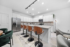 Eine moderne Küche mit weißen Schränken, einem Edelstahl-Kühlschrank, einer Mikrowelle und einer Bar mit Hockern.
