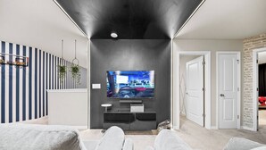 Uma sala de estar moderna com uma televisão de tela plana fixada em uma parede escura, sofás cinzas e uma decoração de parede listrada.