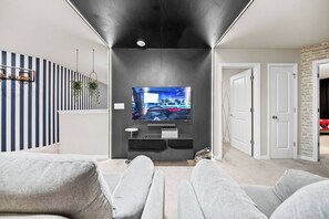 Ein modernes Wohnzimmer mit einem Flachbildfernseher an einer dunklen Wand, grauen Sofas und einer gestreiften Wanddekoration.