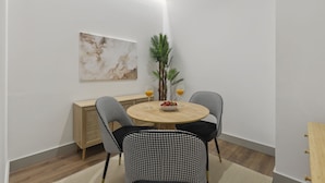 Un comedor con una mesa redonda, dos sillas de estampado pata de gallo, un aparador de madera y una planta en maceta.