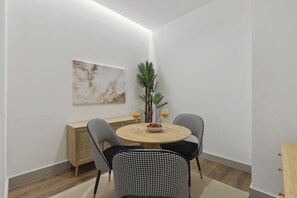 Ein Essbereich mit einem runden Tisch, zwei stuhlig gestreiften Sesseln, einem Holzschrank und einem Blumentopf.