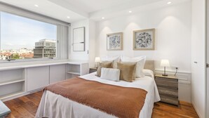 Un dormitorio moderno con una cama grande, un escritorio y vistas a la ciudad.