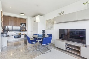 A modern kitchen with dark wood cabinets, a built-in oven, and a dining area with a round table and blue chairs. - Modern 1-Bed Apartment with Panoramic Views (Madrid)