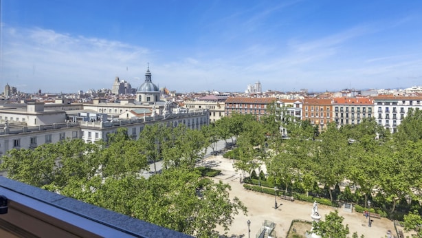 Un paisaje urbano con una cúpula destacada y una estatua en una plaza central rodeada de árboles.