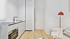 Eine moderne Küche mit weißen Schränken, einem Einbauofen und einem Spülbecken. Eine Tür führt in einen weiteren Raum, und eine rote Stehlampe steht dort.