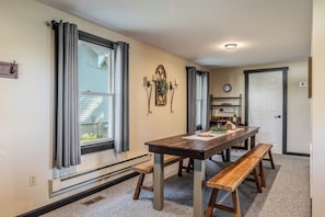 A dining area with a wooden table and benches, a window with curtains, a wall-mounted clock, and a radiator. - Lake View Lodge on Dewart Lake/1 mile from Blue Barn Berry Farm/kayaks! (Syracuse)