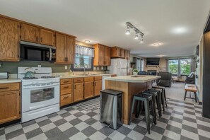 A modern kitchen with wooden cabinets, a stainless steel refrigerator, a built-in oven, and a bar area with stools. - Lake View Lodge on Dewart Lake/1 mile from Blue Barn Berry Farm/kayaks! (Syracuse)