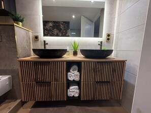 A modern bathroom with a wooden vanity, two black sinks, a mirror above, and a towel storage unit below. - 15 minutes from Futuroscope! Beautiful two-bedroom house, ideal for families (Naintré)