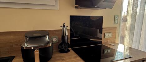 A modern kitchen with a coffee maker, a TV, and a window with a view of trees.