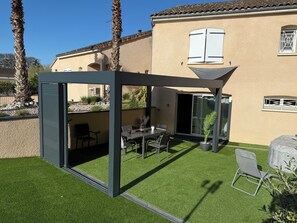 A modern outdoor patio with a glass enclosure, a dining table, chairs, and a small potted plant. - 15 minutes from Futuroscope! Beautiful two-bedroom house, ideal for families (Naintré)