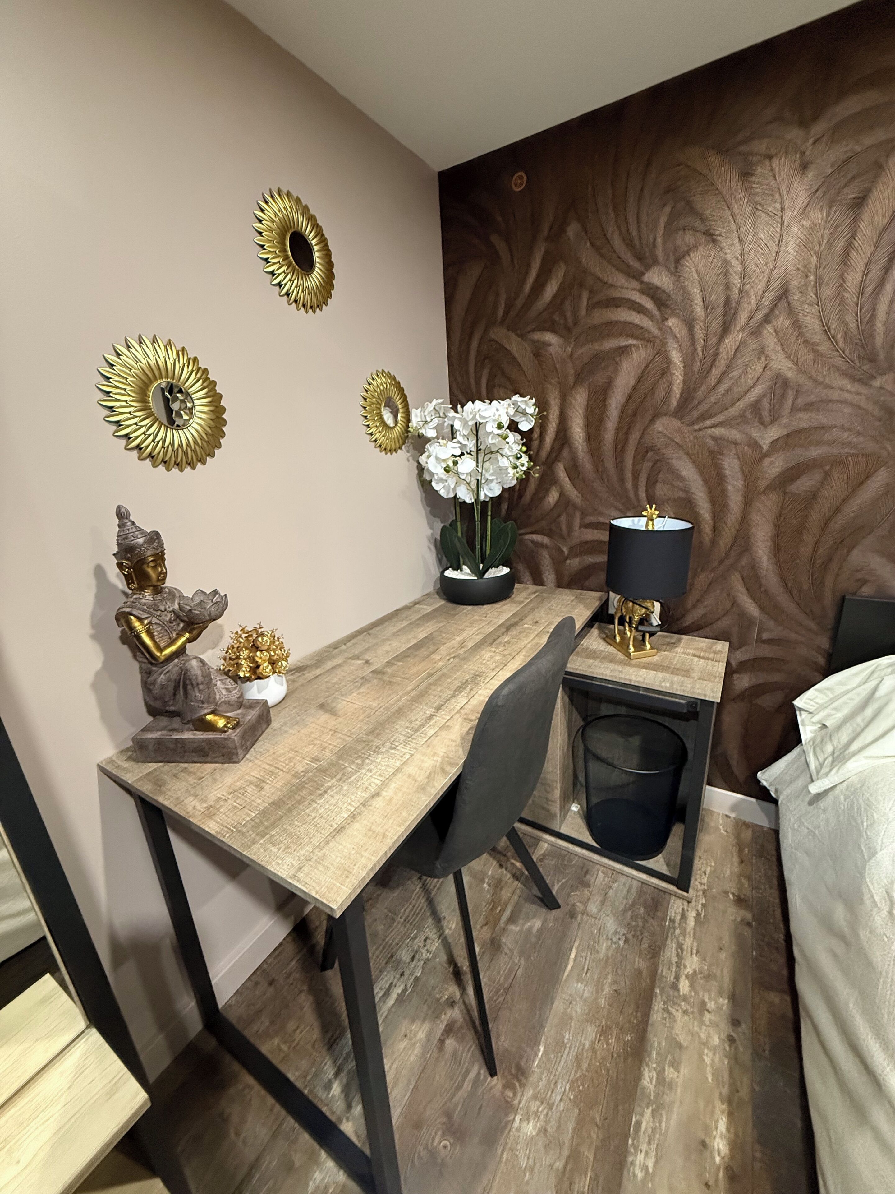 A modern dining area with a wooden table, black chairs, and decorative items including golden sunburst mirrors and white orchids.