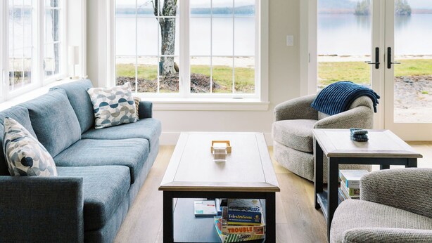 A living room with a sofa, armchair, coffee table, and a view of a lake through large windows. - Luxury Roxbury Pond Lakefront (Roxbury)