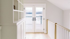 A hallway with white walls, a wooden floor, and a view of a lake through a glass door. - Luxury Roxbury Pond Lakefront (Roxbury)